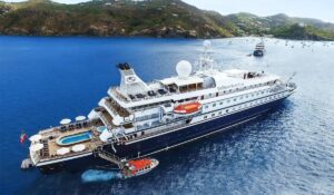 Aerial view of a SeaDream Yacht Club ship anchored in a tropical bay, with a small pool on deck and hills in the background.