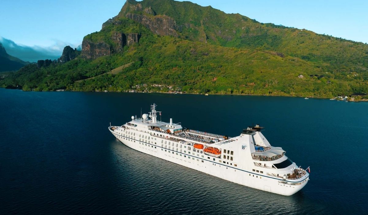 Windstar cruise ship sailing in calm blue water with lush green mountains in the background.