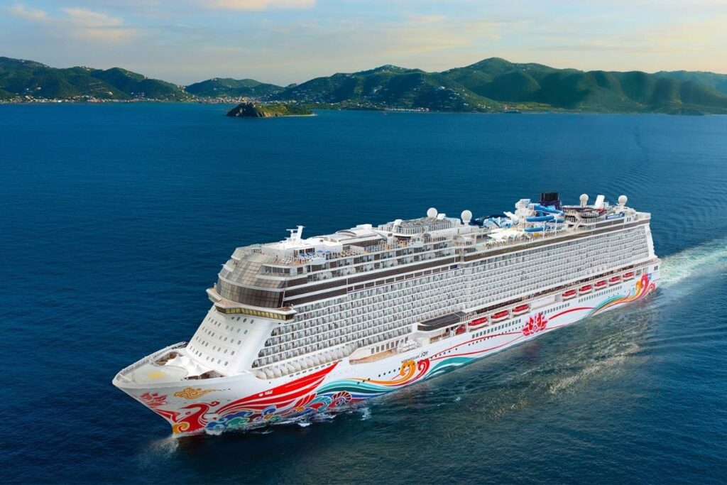 Norwegian Joy cruise ship sailing at sea with colorful hull artwork and green Caribbean islands in the background.