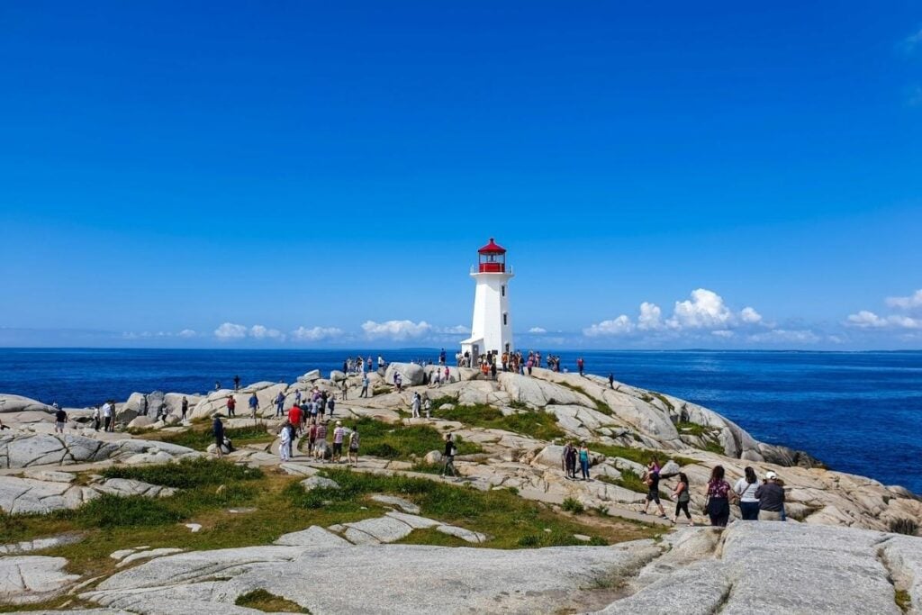 Peggy's Cove Lighthouse in Nova Scotia, Canada, surrounded by rocky coastline and tourists overlooking the Atlantic Ocean.