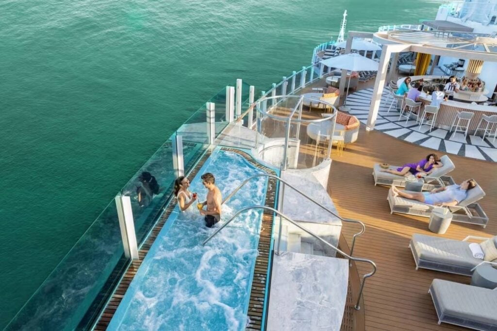 Vibe Beach Club aboard Norwegian Bella, featuring an oceanfront infinity hot tub, lounge chairs, and an outdoor bar overlooking the sea.