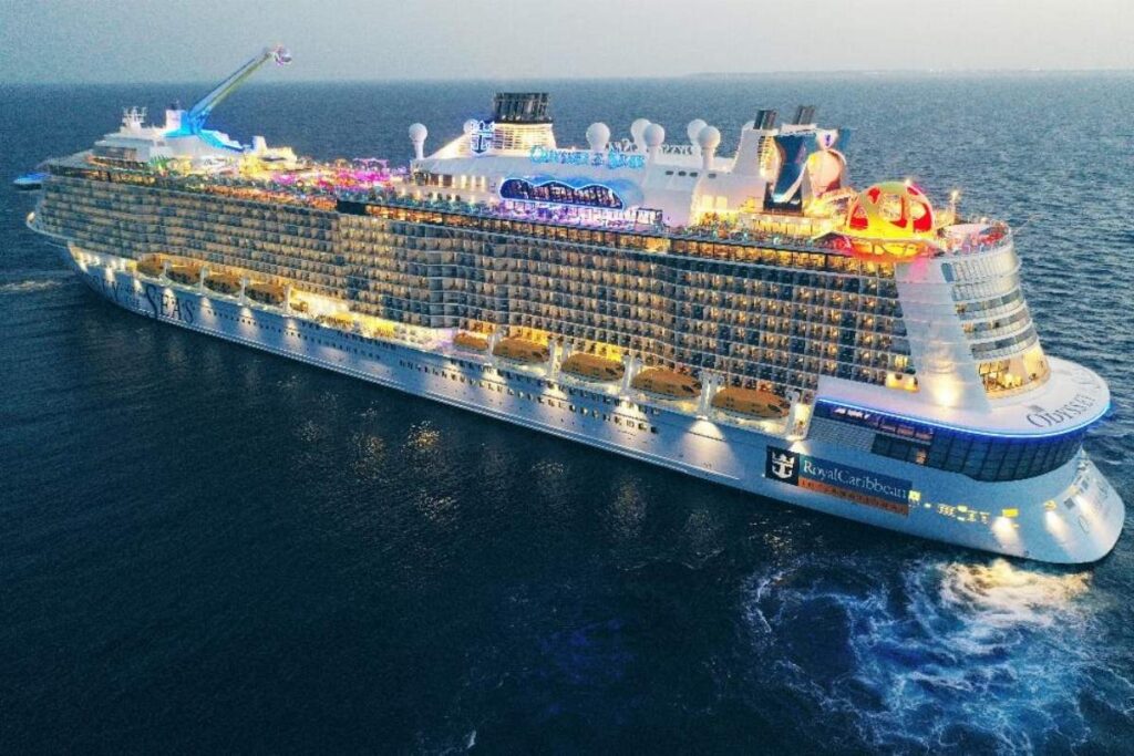 Aerial view of Royal Caribbean's Odyssey of the Seas sailing at dusk, with illuminated upper decks and ocean views.