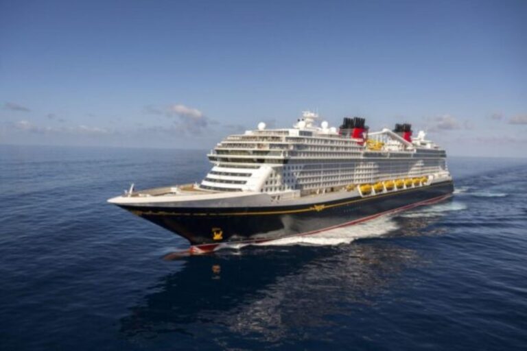 Disney Treasure cruise ship sailing through the ocean, showing its black hull, white decks, yellow lifeboats, and red funnels.