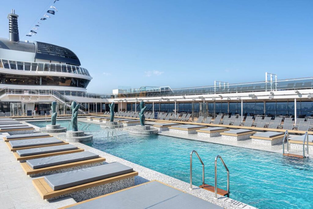 The Atmosphere Pool on MSC Euribia boasts a tranquil setting with crystal clear water, flanked by stylish sun loungers and elegant sculptures, under a vast open sky, inviting relaxation and leisure on the sun-drenched deck.