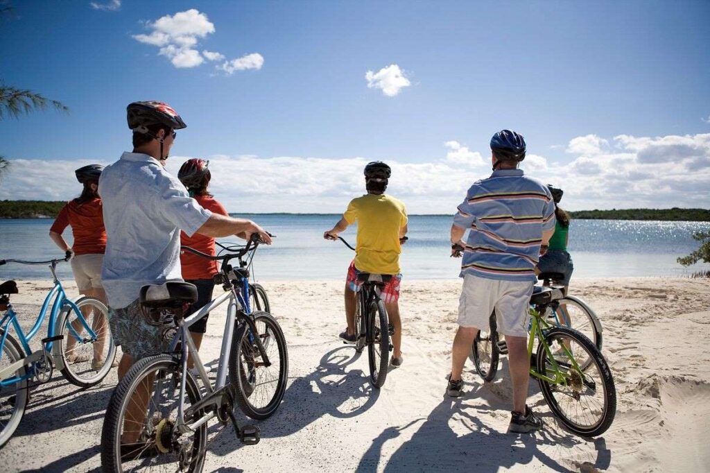 A group of cyclists with helmets on, pausing during their bike tour to enjoy the scenic views at Half Moon Cay, with the clear blue sky above and the tranquil sea in the background.