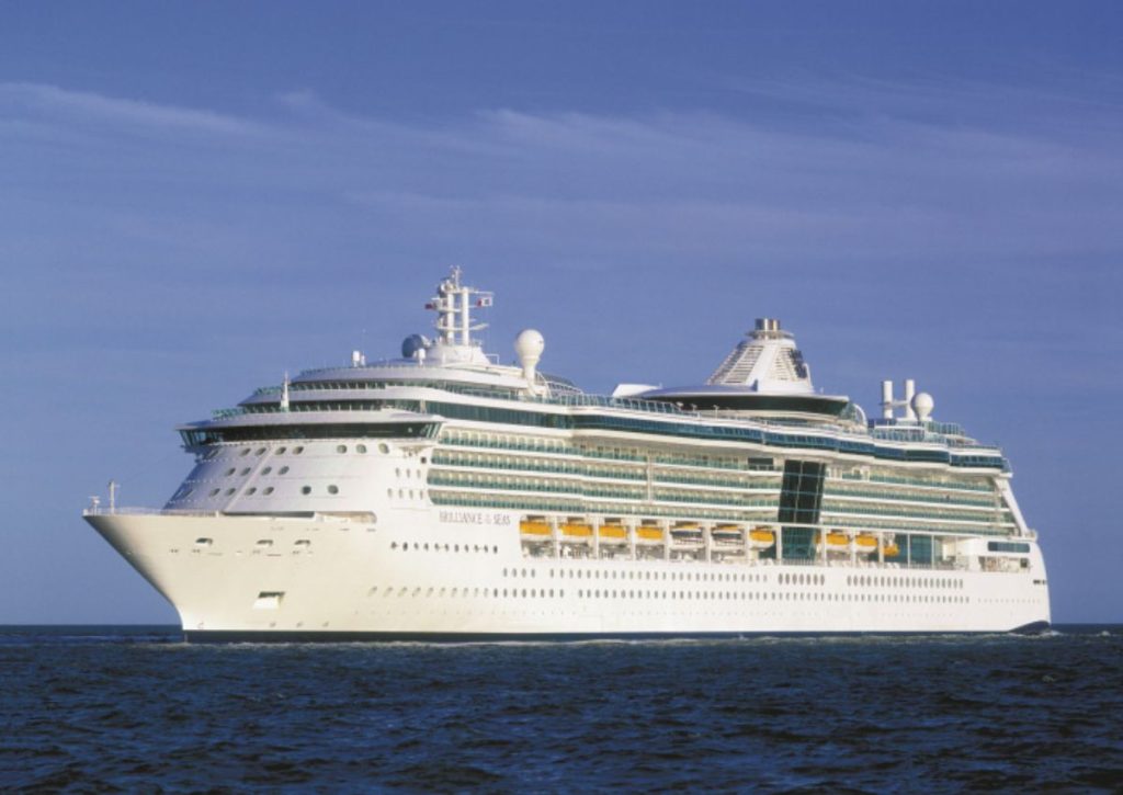 The Brilliance of the Seas cruise ship, a part of the Royal Caribbean fleet, glides across calm ocean waters under a clear blue sky, reflecting the sunlight off its many windows and balconies.