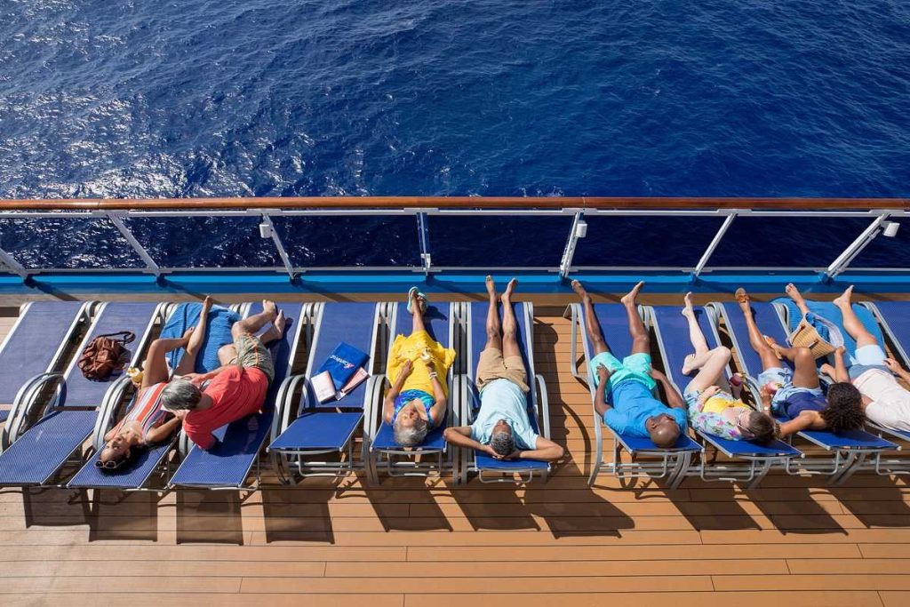 Guests relaxing on sun loungers on the deck of the Carnival Horizon cruise ship, basking in the sun with a clear view of the deep blue sea alongside