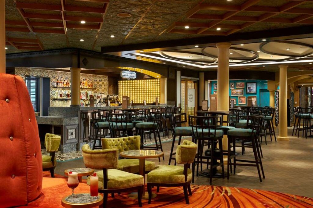 The Havana Bar on Carnival Celebration exudes a cozy and sophisticated charm with its eclectic mix of plush vintage-style seating, warm lighting, and a rich color palette, inviting guests to unwind in a space reminiscent of a classic Cuban lounge.
