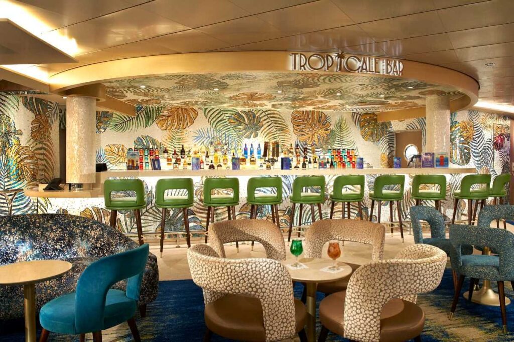 The Tropicale Bar on Carnival Celebration, adorned with a stunning mosaic backdrop of tropical foliage, offers a vibrant setting with green bar stools and patterned armchairs, perfect for enjoying a refreshing cocktail in a lively, stylish atmosphere.