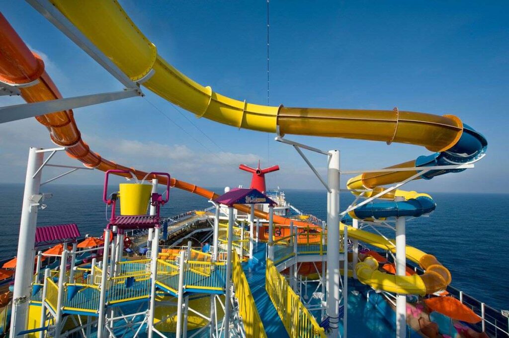 The Splash Zone on Carnival Magic boasts an array of colorful water slides arching gracefully over the sun-drenched deck, against the backdrop of a calm blue sea.