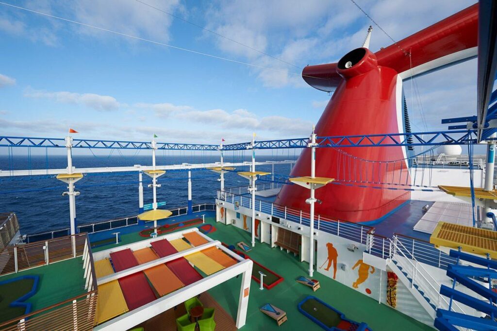 The expansive Ropes Course on Carnival Panorama, featuring an adventurous high-elements course with views of the sea, alongside a colorful mini-golf course and relaxation area under the ship's iconic red funnel.