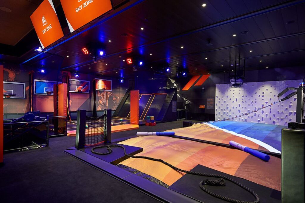 The Sky Zone indoor trampoline park and challenge zone on Carnival Panorama, featuring a vibrant climbing wall, basketball hoops, and activity courts, all under dynamic lighting for an energetic atmosphere.