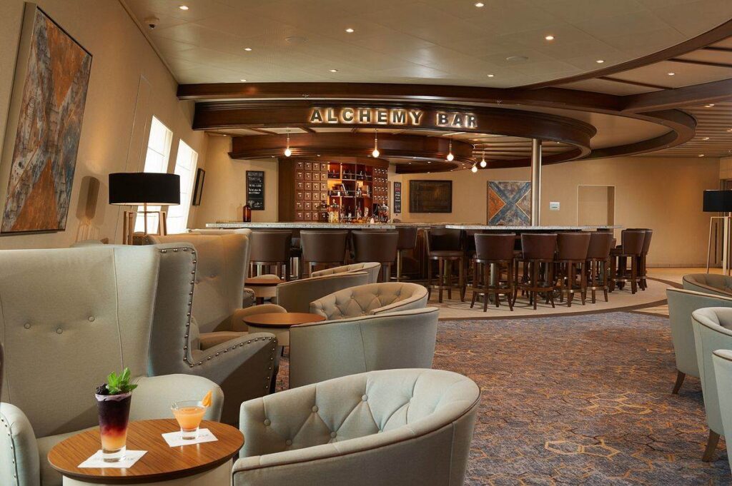 The sophisticated Alchemy Bar on Carnival Sunrise, showcasing a relaxed lounge atmosphere with plush seating, an elegant bar setup, and modern art, perfect for sipping crafted cocktails.