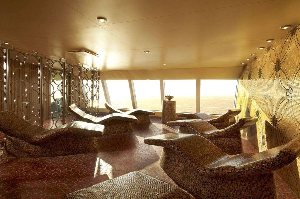 The serene tepidarium of Cloud 9 Spa on Carnival Breeze, bathed in golden light with a row of heated loungers overlooking the tranquil sea.