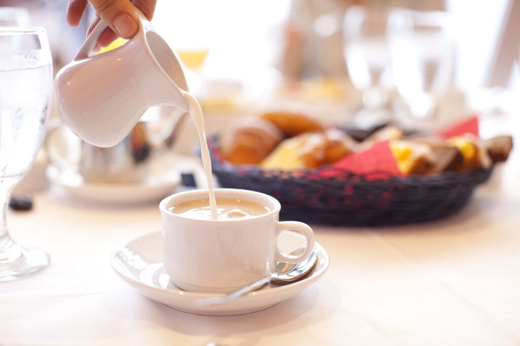 A close-up of a creamy coffee being poured during Seaday Brunch on a Carnival Cruise, with a basket of assorted pastries in soft focus in the background, inviting a leisurely morning.