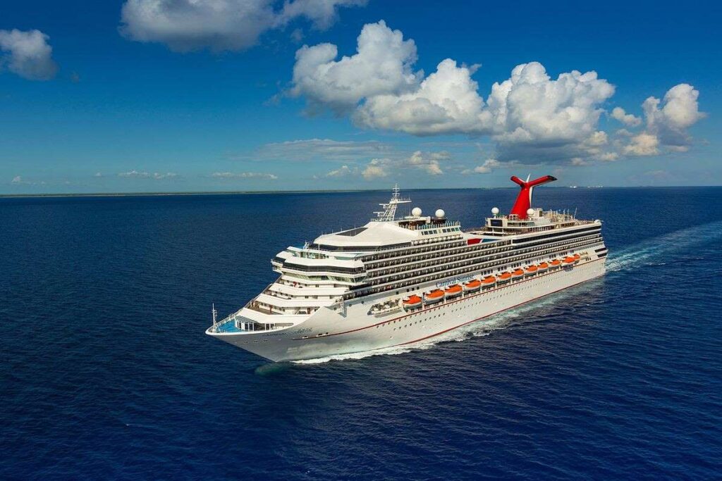 The Carnival Sunrise cruise ship sails on a calm ocean, its red funnel iconic against the vast blue sky scattered with white clouds, embodying a sense of adventure on the high seas.