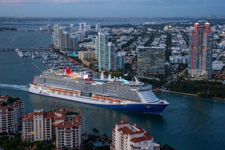 Aerial view of the Carnival Celebration cruise ship docked in Miami at twilight, with the city's skyline and densely packed high-rises in the background.