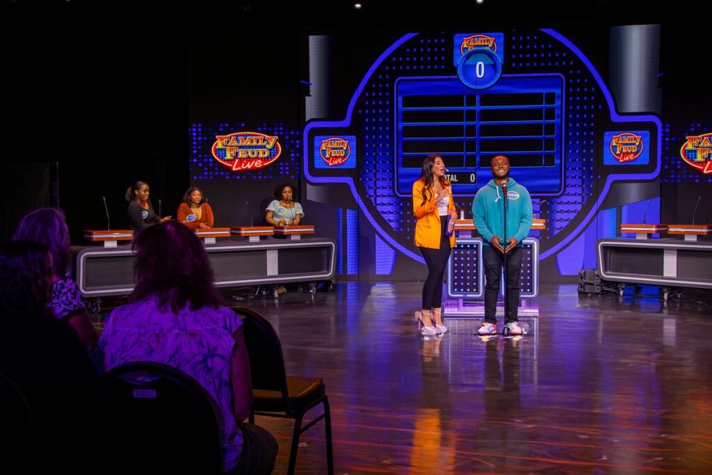 Contestants eagerly participate in Family Feud Live on a Carnival Cruise, showcasing the iconic game show set with bright, colorful lights and an excited audience watching the friendly competition.