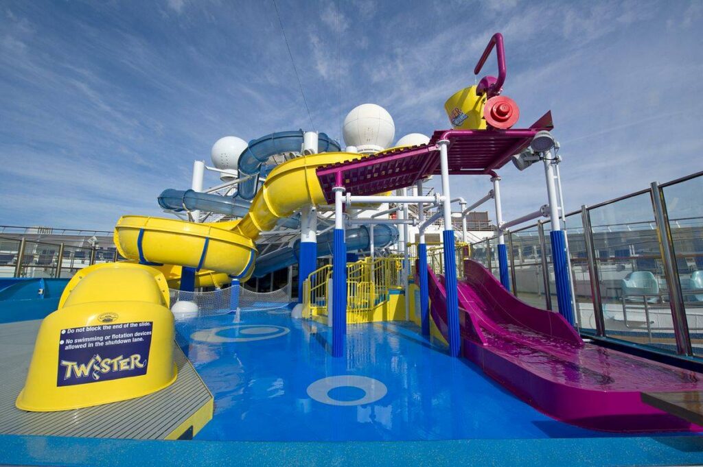 WaterWorks on Carnival Glory under a clear blue sky, featuring vibrant yellow and purple water slides and splash areas for a fun-filled aquatic adventure at sea.
