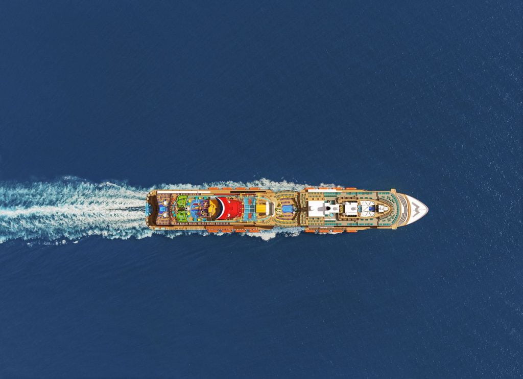 Aerial view of a colorful cruise ship cutting through the deep blue waters, creating a white wake behind it