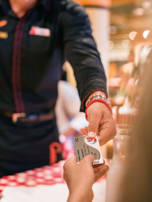 Close-up of a guest receiving a Carnival VIFP Club card from a crew member, highlighting the personalized service aboard the Carnival Breeze cruise ship.