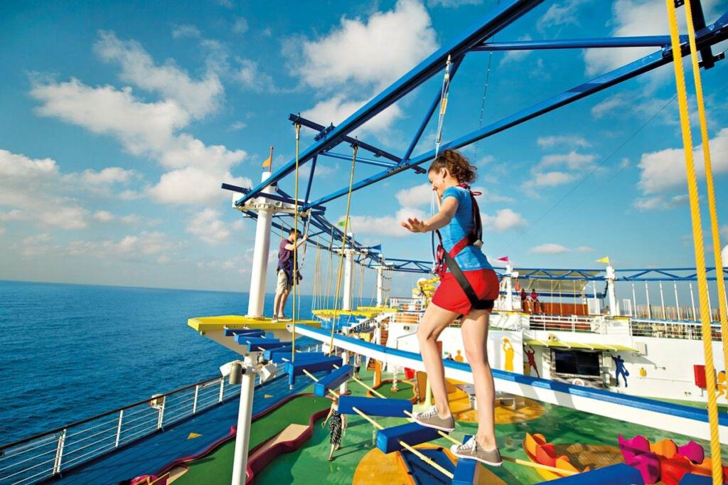 An adventurous guest navigates the high ropes of the SkyCourse on Carnival Breeze, with the expansive blue ocean and clear skies in the background, adding an element of thrill to the cruise experience.