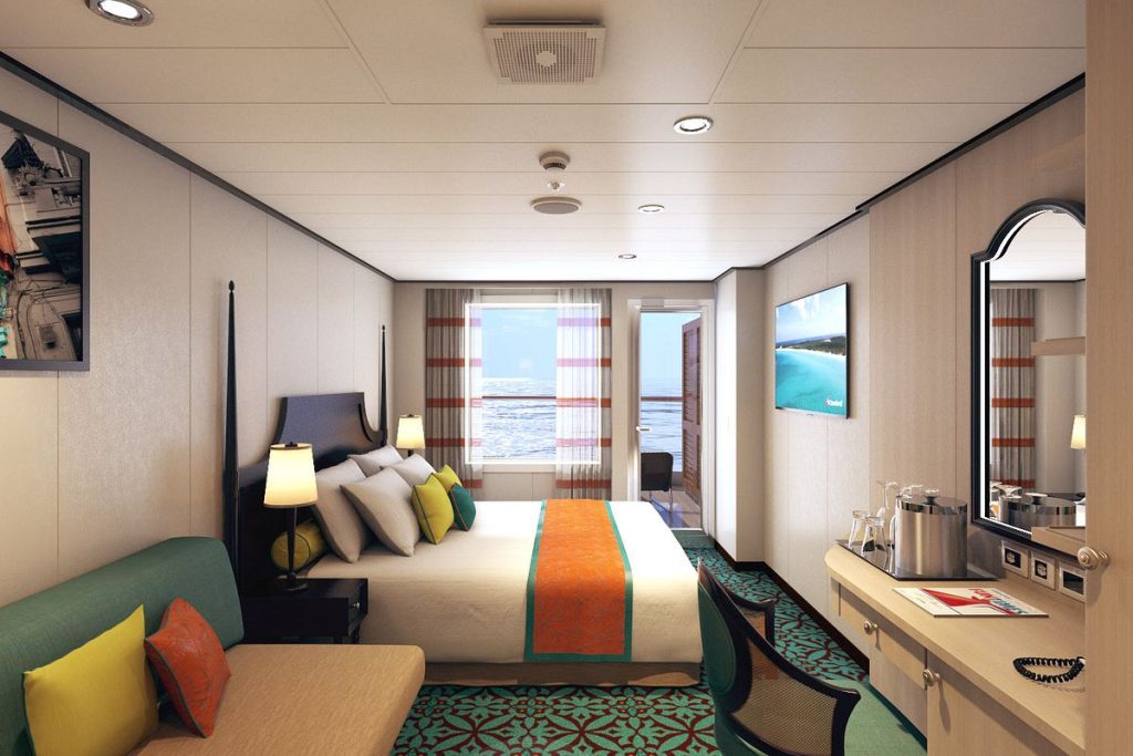 Cozy and modern extended balcony stateroom on Carnival cruise, with a comfortable bed, bright decorative pillows, and a view of the ocean through the window.