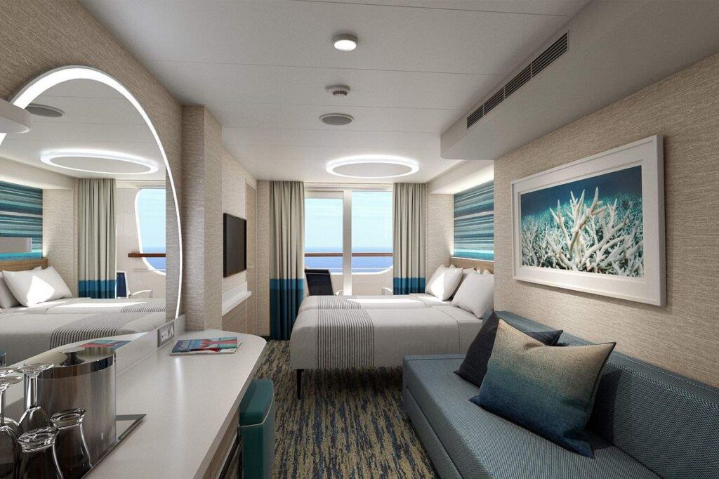 A Cove Balcony stateroom on Carnival Celebration, featuring a serene color palette with ocean-inspired art, offers a restful ambiance with a comfortable bed, a cozy seating area, and a private balcony that opens up to sweeping sea views, blending indoor luxury with the beauty of the sea.