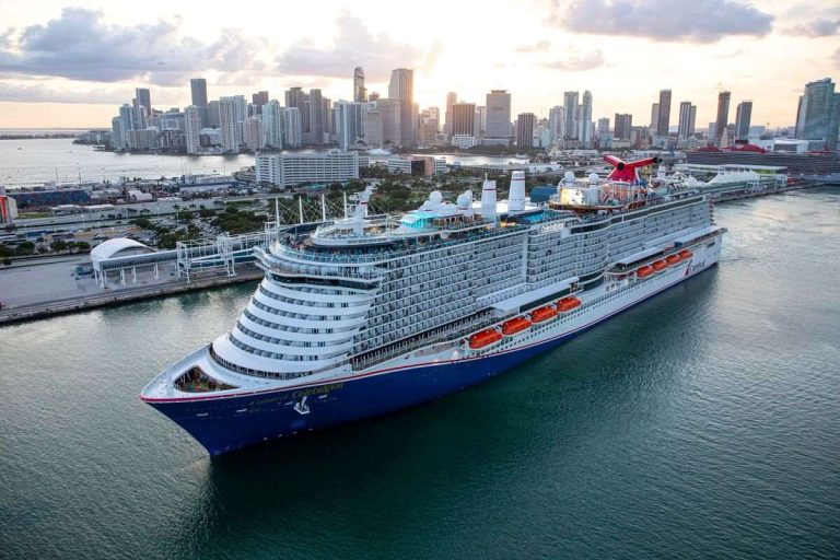 Carnival Celebration cruise ship docked in the Port of Miami with the city's skyline in the background during a sunset.