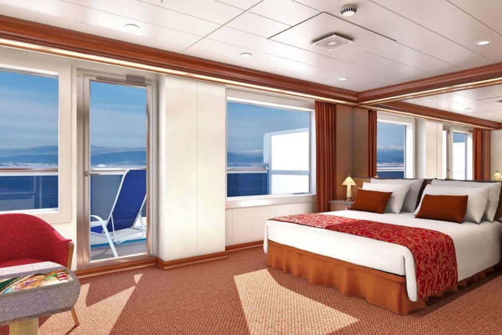 An elegantly furnished Grand Suite on the Carnival Dream cruise ship, featuring a large comfortable bed with white and red bedding, a sitting area with a red armchair, and a private balcony overlooking the serene ocean.