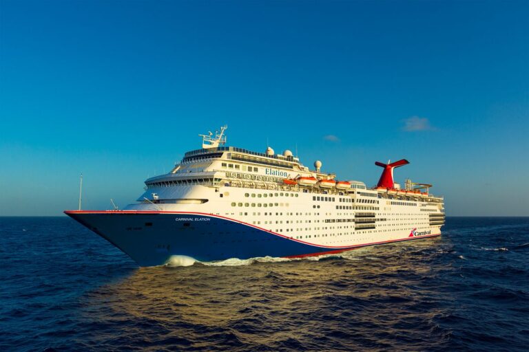 The image displays the 'Carnival Elation' cruise ship, easily recognizable by its distinctive red funnel and white-and-blue hull, sailing on a serene blue ocean under a clear sky. Perfect for a vacation getaway theme.