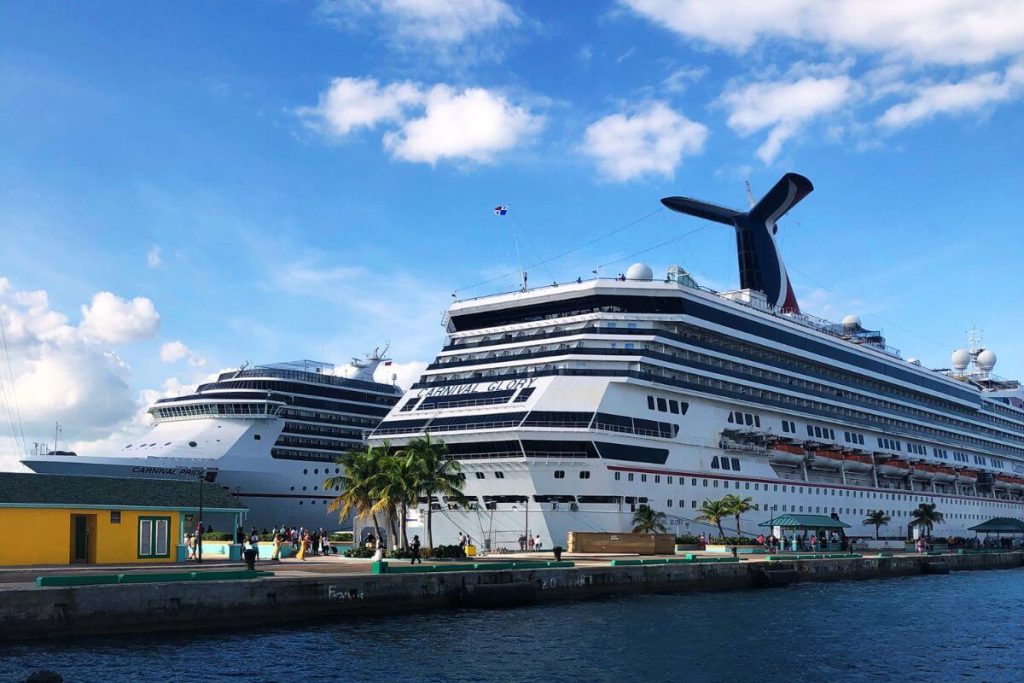 Carnival Glory and Carnival Pride cruise ships docked side by side under a clear blue sky, with passengers strolling on the quay.