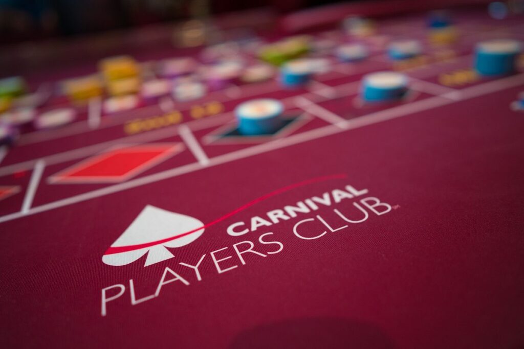 Close-up of a vibrant casino table with the 'Carnival Players Club' logo prominently displayed, surrounded by colorful betting chips blurred in the background, capturing the excitement of gaming aboard a Carnival cruise.