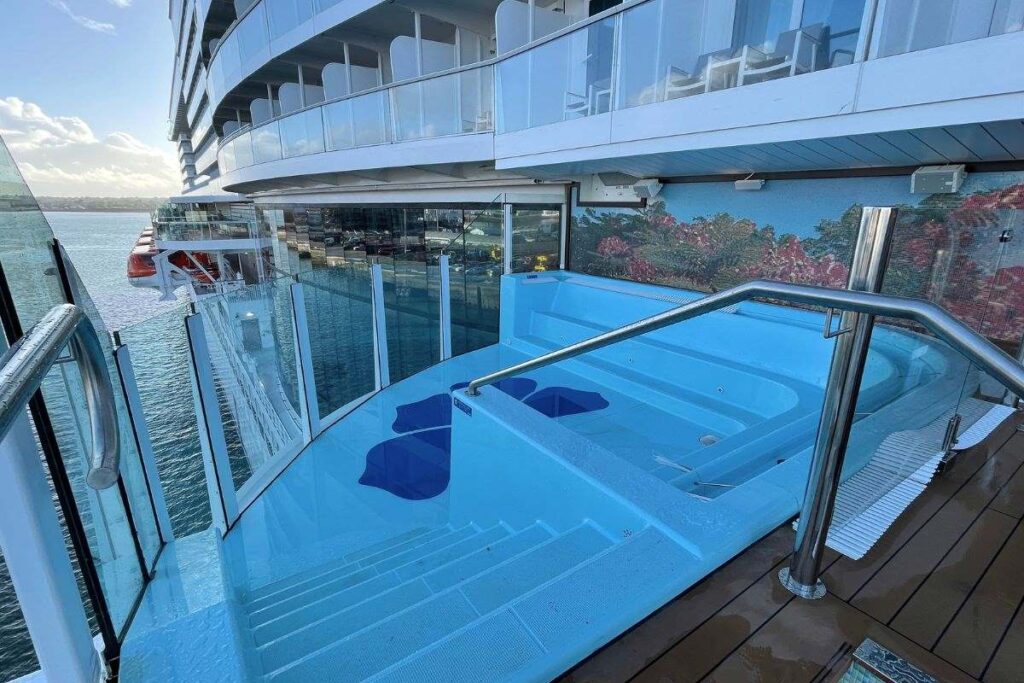 This image depicts the Havana Pool on a Carnival cruise ship, showcasing a private, glass-enclosed pool area with a clear view of the surrounding ocean. The pool features sleek railings, a few steps leading into the water, and is surrounded by balcony-style seating, creating an exclusive and relaxing atmosphere for passengers.