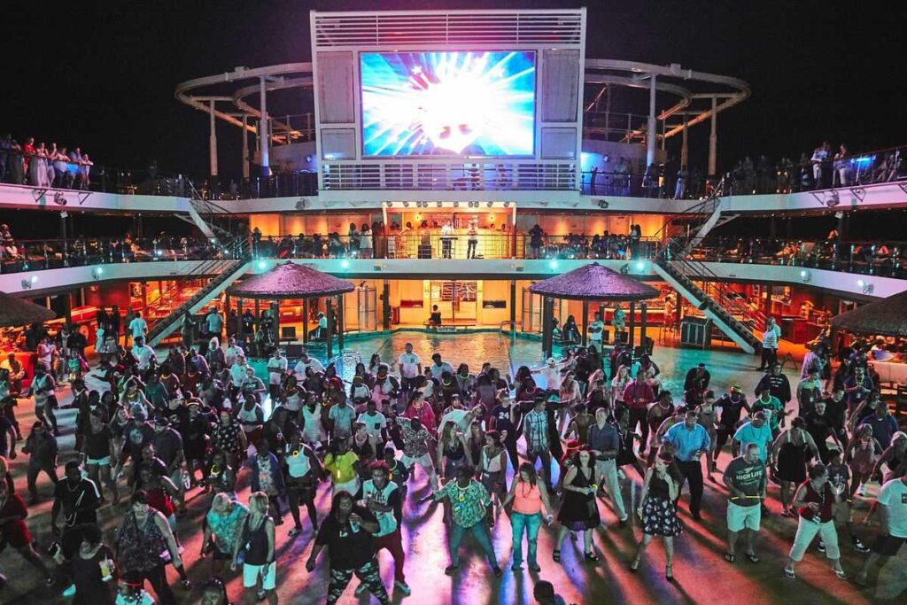Vibrant Lido Deck party in full swing on Carnival Vista, with guests dancing under the night sky as the large screen illuminates the deck with colorful visuals.