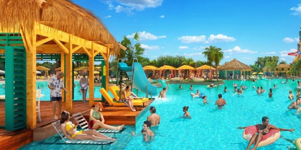 A vibrant scene at Celebration Key in The Bahamas shows people lounging, swimming, and enjoying a sunny day at a large resort-style pool. The pool area includes a thatched-roof cabana, waterslide, colorful loungers, and yellow umbrellas, with guests relaxing in floats and sipping drinks under a bright blue sky.