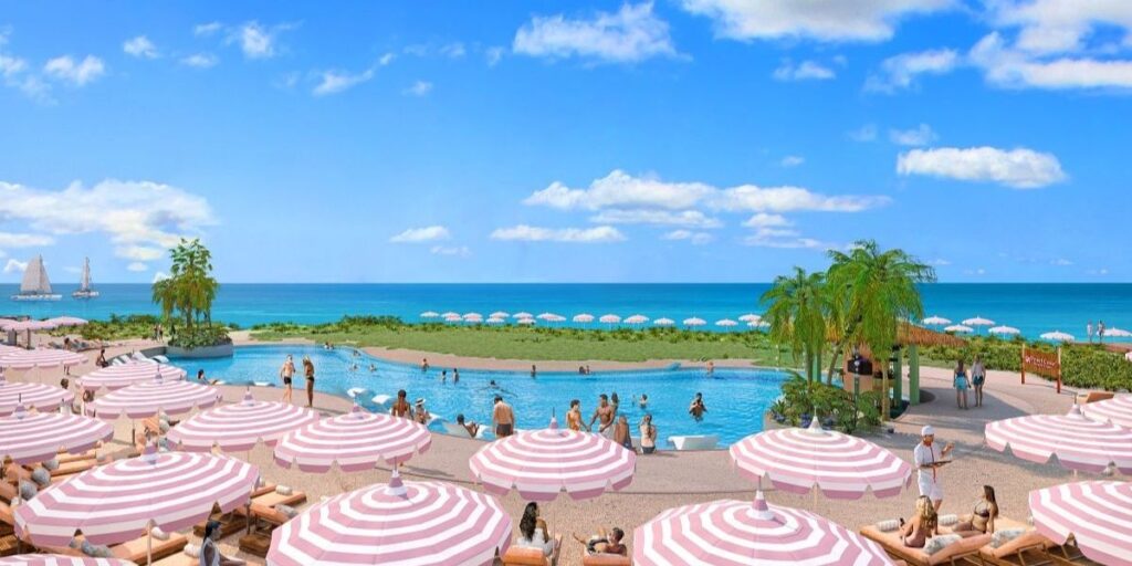 Guests relax under pink and white striped umbrellas at Celebration Key's beachfront pool, with ocean views stretching to the horizon and sailboats in the distance. The scene features a large, curving pool, tropical landscaping, and a laid-back atmosphere perfect for sunbathing and seaside lounging.