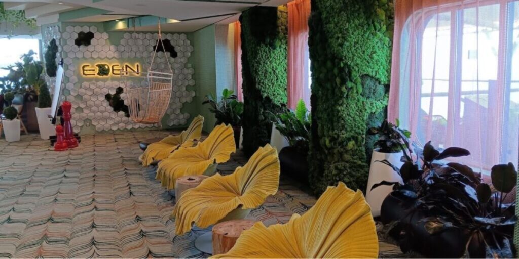 The Eden lounge on the Celebrity Apex cruise ship, featuring vibrant, nature-inspired decor with lush green walls and unique seating resembling large yellow leaves. The area includes a hanging wicker chair and various plants, creating a relaxing and immersive atmosphere for guests.