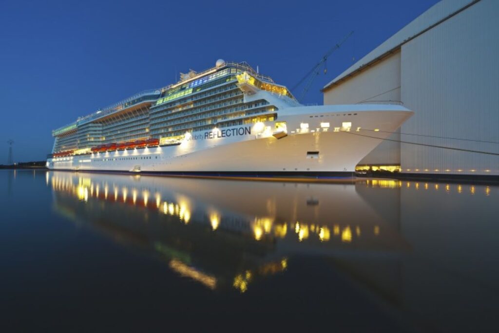 This image features the Celebrity Reflection cruise ship docked at night, with its bright lights reflecting beautifully on the calm water. The ship’s name, "Celebrity Reflection," is illuminated on its white hull, standing out against the dark evening sky. The soft glow of the ship’s lighting creates a serene, majestic atmosphere, highlighting the elegance of the vessel as it rests in the harbor.