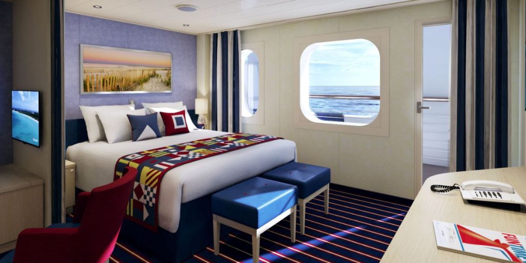 A cozy Cove Balcony Family Harbor Suite with a nautical theme, featuring a comfortable queen-size bed adorned with a colorful geometric-patterned blanket. The suite includes a red chair, a blue ottoman, and maritime-inspired art above the bed. A round porthole window offers a view of the ocean, complementing the room's inviting and family-friendly atmosphere.