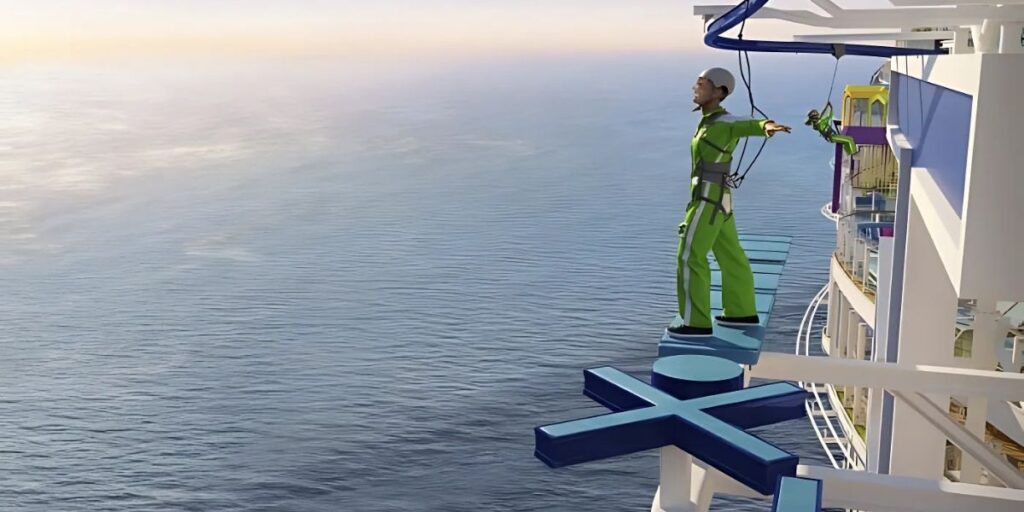 A person in a neon green safety suit and helmet balances on a narrow platform suspended high above the ocean, connected by a harness to the side of Royal Caribbean’s Star of the Seas. The daring skywalk experience, part of the ship’s new Thrill Island area, features steps shaped like the cruise line’s crown-and-anchor logo extending out over open water.