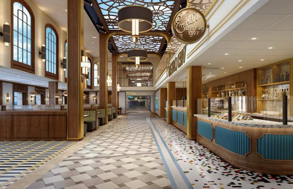 The image is of Emeril's Bistro 1396 located on Carnival Celebration, featuring a sophisticated and welcoming dining space. The design carries a modern take on classic bistro aesthetics, with tall arched windows, wood paneling, and decorative ceiling elements. The central pathway with its geometrically patterned flooring guides guests through the space, while the counters on either side display a variety of enticing culinary offerings under warm, elegant lighting fixtures. The venue exudes a sense of contemporary elegance combined with casual dining comfort.