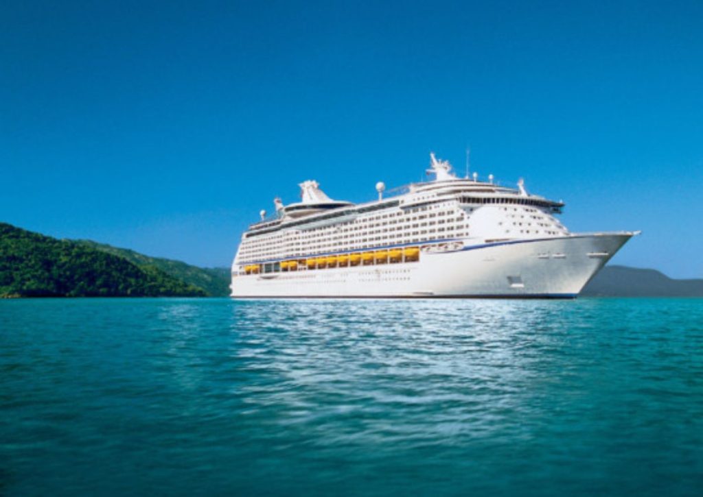 Royal Caribbean's Explorer of the Seas cruise ship in a serene setting, surrounded by the tranquil turquoise waters of a bay with lush green hills in the background under a clear blue sky.
