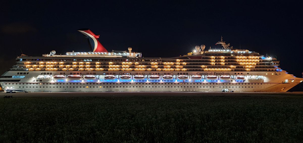 The Carnival Freedom cruise ship illuminated at night, showcasing the vessel's multiple decks and rows of balconies. The ship's name is prominently displayed on the side, and the iconic red and blue funnel stands tall against the dark sky, symbolizing the ship's readiness for adventure on the open sea.