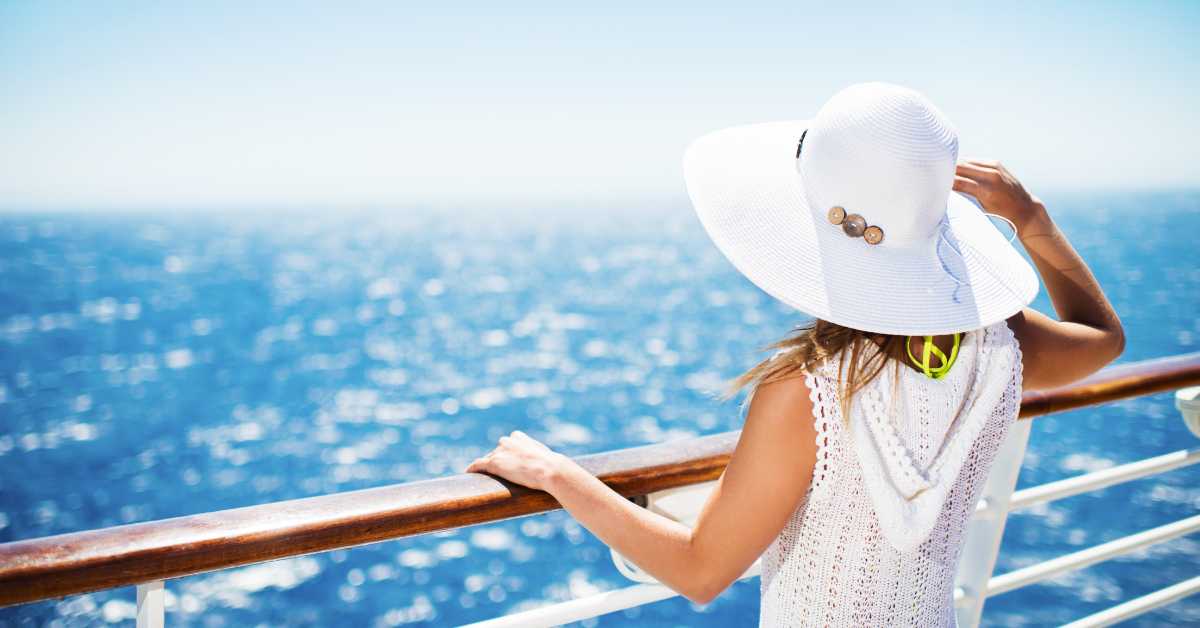 a lady with a white hat standing on the deck of a cruise ship, looking out to sea.