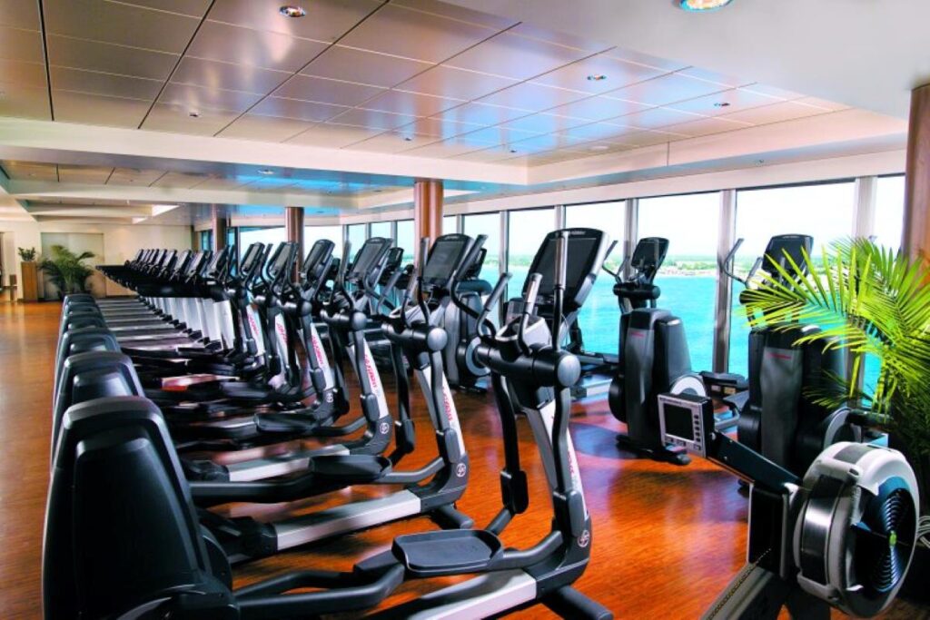 A row of elliptical machines in the Fitness Center on Norwegian Epic, with expansive windows offering serene ocean views, combining exercise with the beauty of maritime travel.