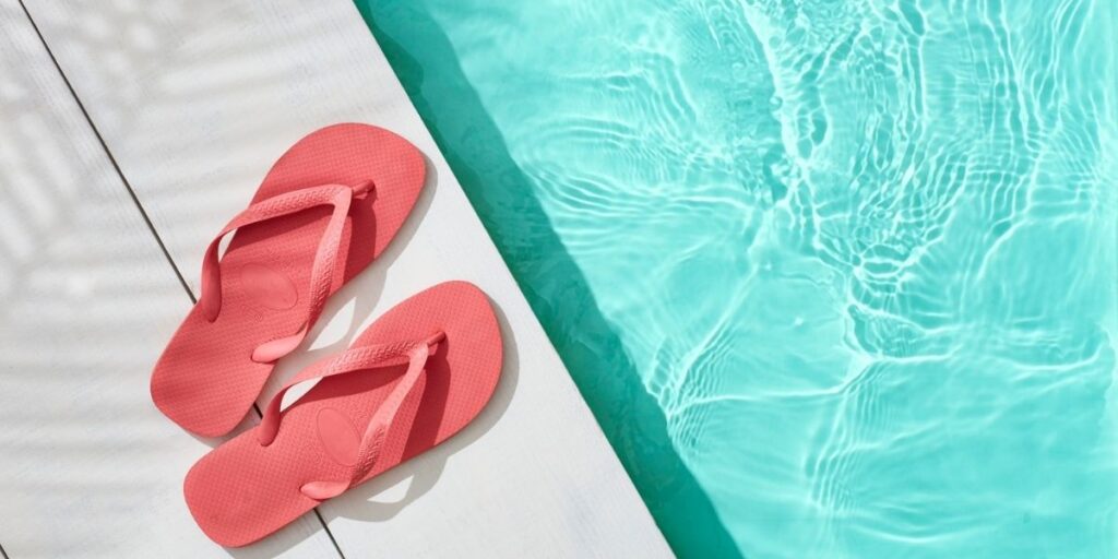 Pink flip-flops resting on a white deck beside a sparkling turquoise cruise ship pool.