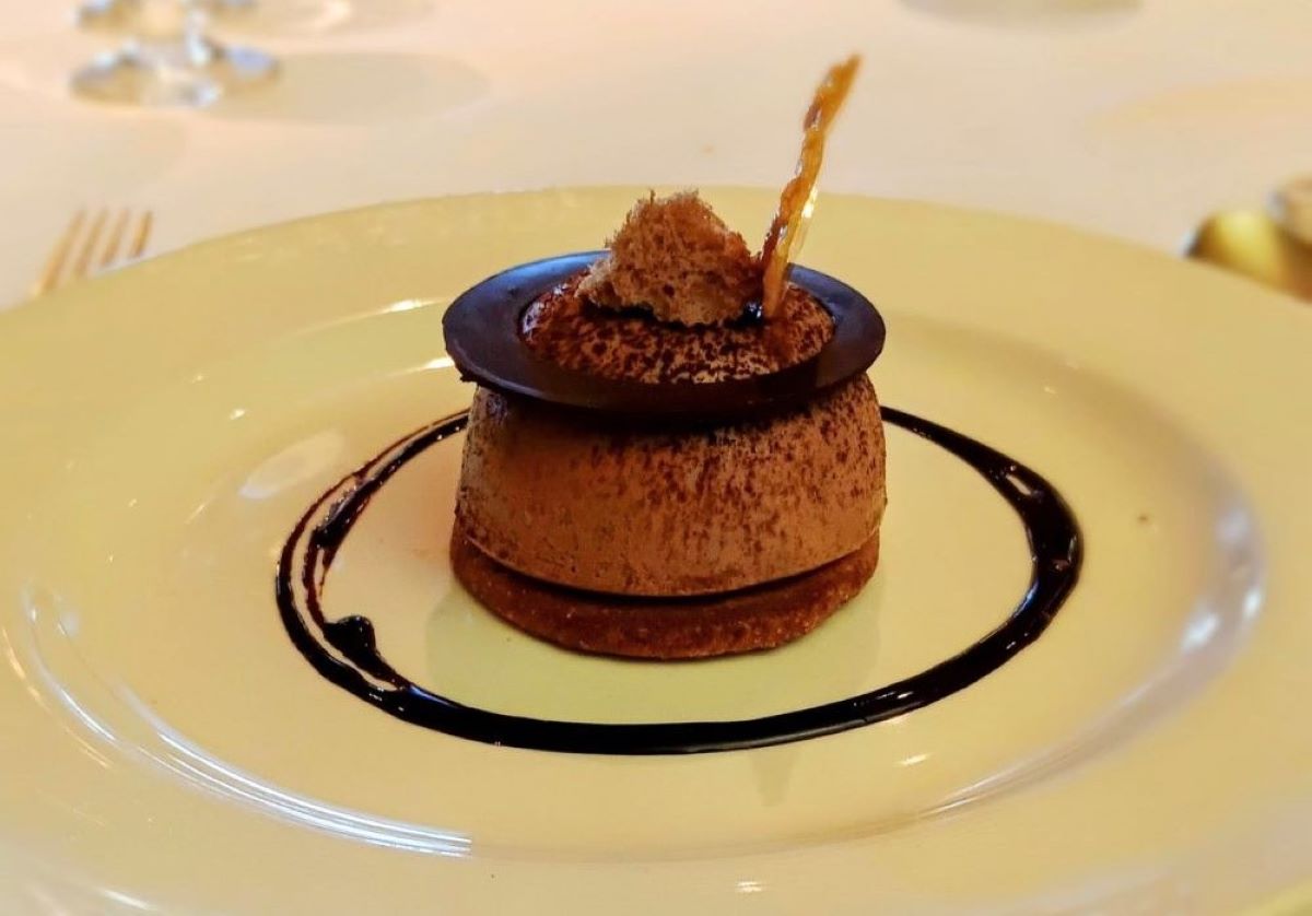 The image displays an elegantly plated dessert served on the Regal Princess cruise ship. The dessert appears to be a chocolate mousse or ganache topped with a decorative chocolate disk and a small garnish. It's set on a thin crust base, with a drizzle of chocolate sauce artfully surrounding it on the plate, making it a visually appealing gourmet treat.
