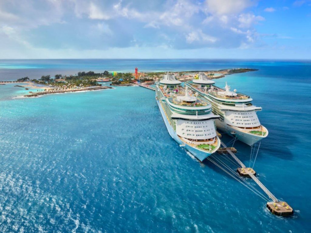 Aerial view of Royal Caribbean's Freedom of the Seas cruise ship docked at a vibrant Caribbean island, with crystal-clear turquoise waters and a bustling pier, illustrating a tropical paradise.