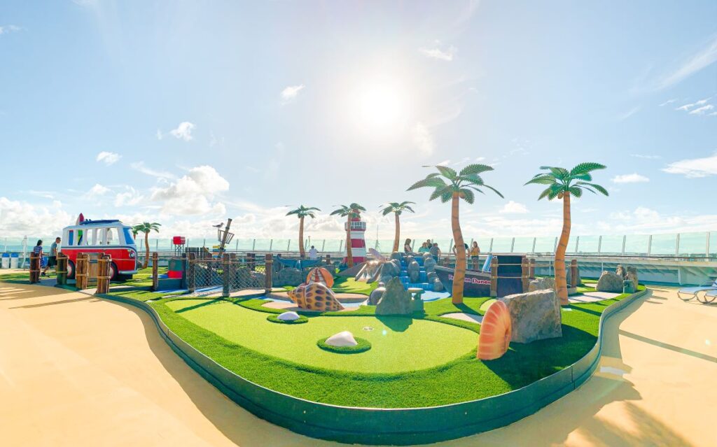 This image features the mini golf course aboard the amplified Freedom of the Seas cruise ship, showcasing a colorful and playful design. The course is adorned with whimsical elements such as palm trees, rocks, and a miniature ship, set under a sunny, blue sky. This family-friendly attraction offers fun and entertainment for all ages in a vibrant outdoor setting.